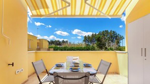 Eine Terrasse im Freien mit Esstisch und Stühlen, darüber ein gelbes Sonnendach.