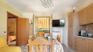 Eine kompakte Küche mit Holzschränken, einem Esstisch mit Stühlen und einem an der Wand befestigten Fernseher.