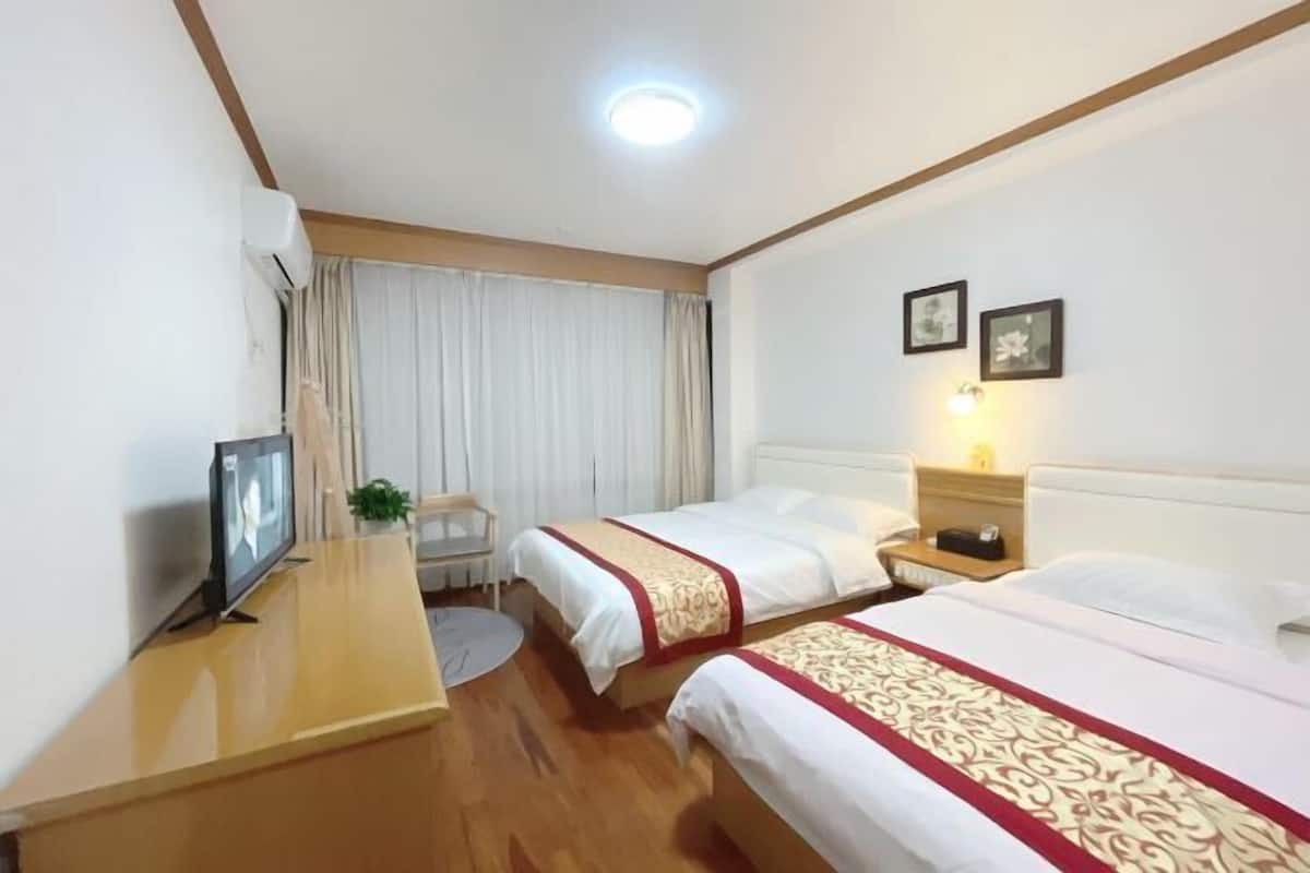A hotel room with two beds, a desk with a TV, a bedside table with a lamp, and a window with curtains.