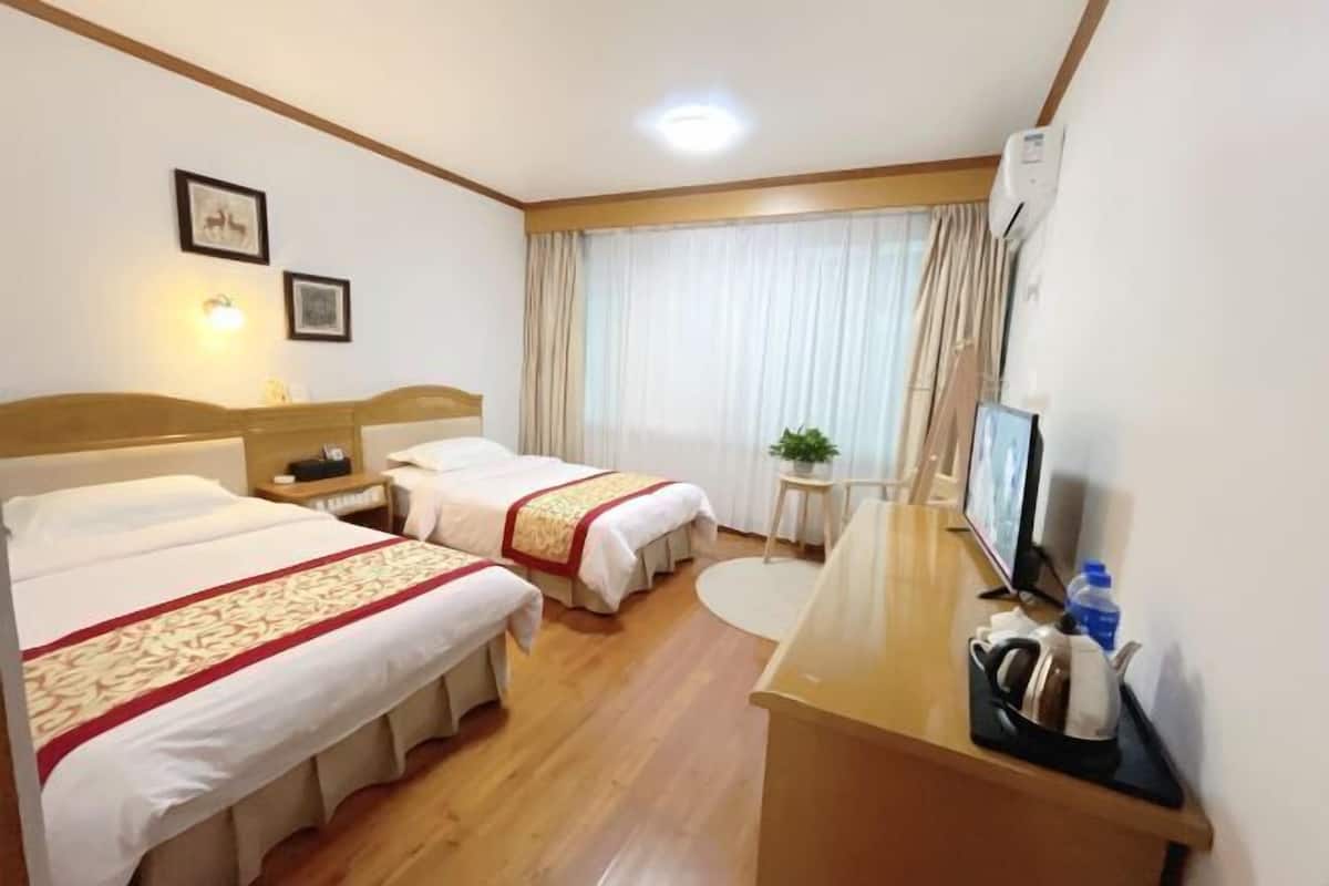 A hotel room with two beds, a desk, a television, and a window with curtains.