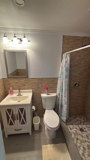 A bathroom with a white sink, mirror, and toilet, a shower with a curtain, and a wooden wall. - Aqua Bond - beautiful direct ocean view home in Rainbow Bay (Rainbow Bay)