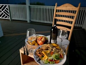 A dining table with plates of food, wine glasses, and a bottle of wine on a wooden deck. - Aqua Bond - beautiful direct ocean view home in Rainbow Bay (Rainbow Bay)