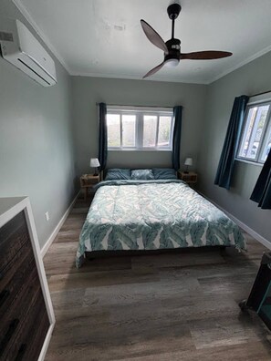 A bedroom with a bed, a ceiling fan, a window with curtains, and a nightstand with a lamp. - Aqua Bond - beautiful direct ocean view home in Rainbow Bay (Rainbow Bay)