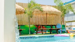 A pool area with a thatched roof, lounge chairs, and inflatable toys. - Home for 15 Guests with Private Pool and Pool Table (Aguadilla)