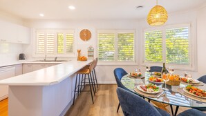 A modern kitchen with a central island, bar stools, and a dining table set for a meal. - Tomaree Mews 5, 18 Tomaree St - Stunning townhouse in the heart of town (Nelson Bay)