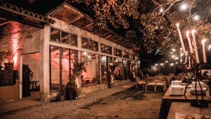 A rustic building with large windows, outdoor seating, and string lights.