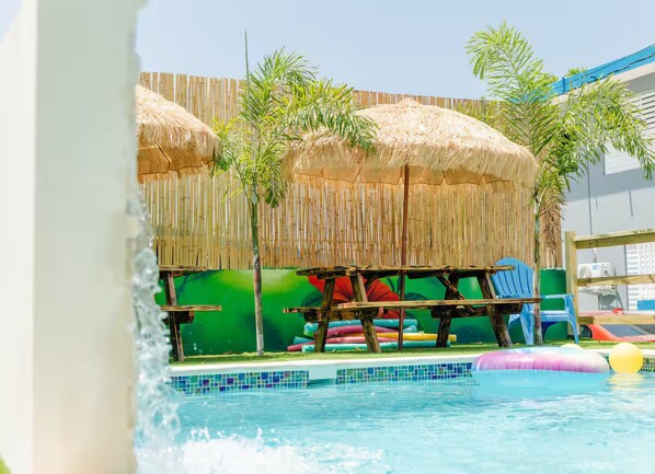 Un área de piscina con techo de paja, sillones de descanso y juguetes inflables.
