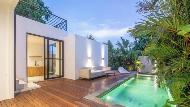 Un espace de vie extérieur moderne doté d’une piscine, d’une terrasse en bois et d’un mur extérieur peint en blanc.