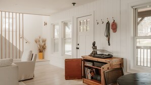 A room with a wooden floor, white walls, a white door, a white sofa, a small wooden table, and a window with a view.