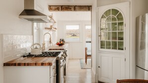 A kitchen with a wooden countertop, white cabinetry, a stove, and a view through a window.