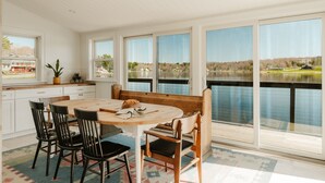 A dining area with a wooden table and chairs, a bench, and large windows overlooking a body of water.