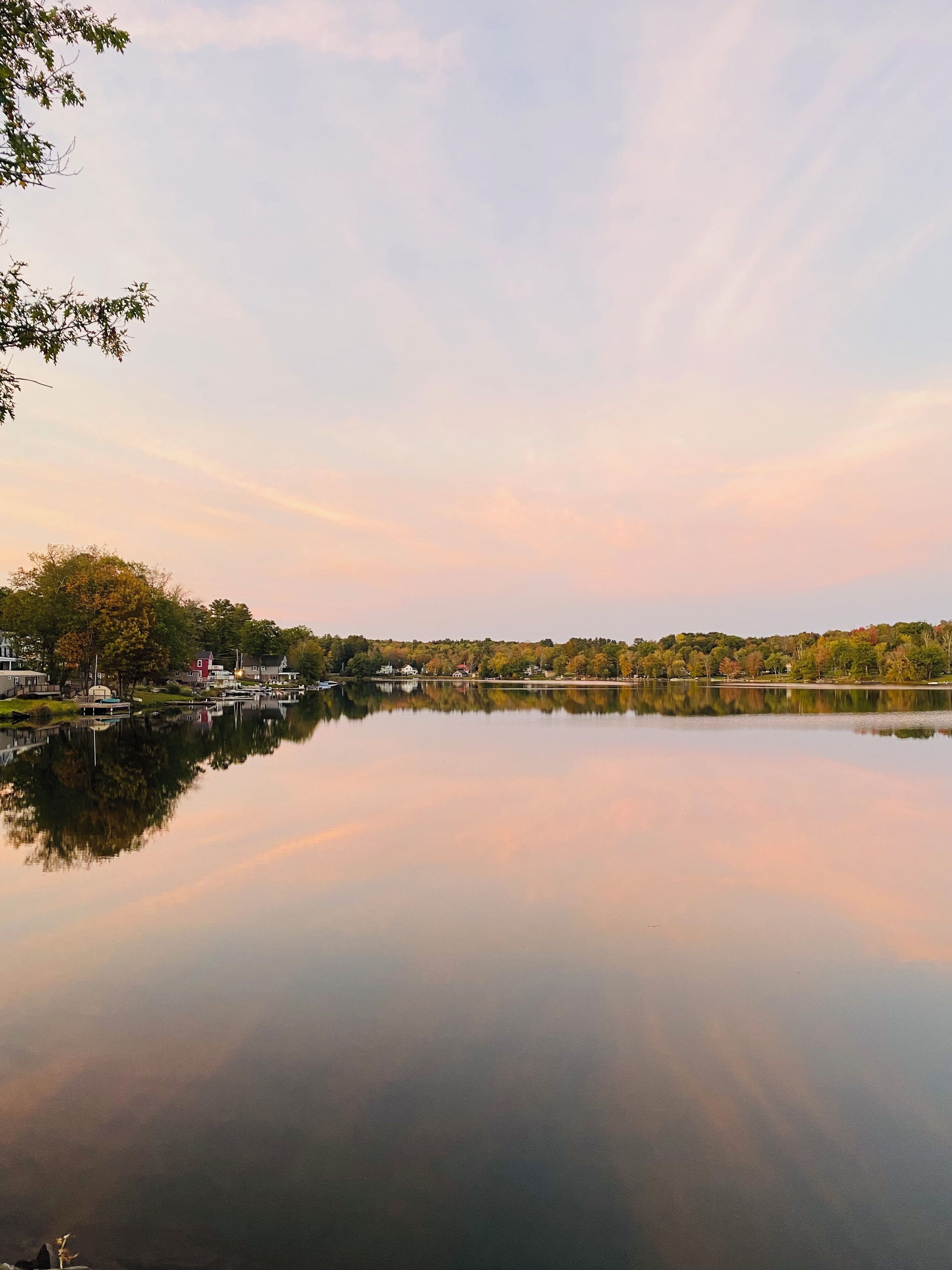 Un lac paisible dont les eaux reflètent les arbres et les bâtiments, le tout étant entouré d’une zone boisée.
