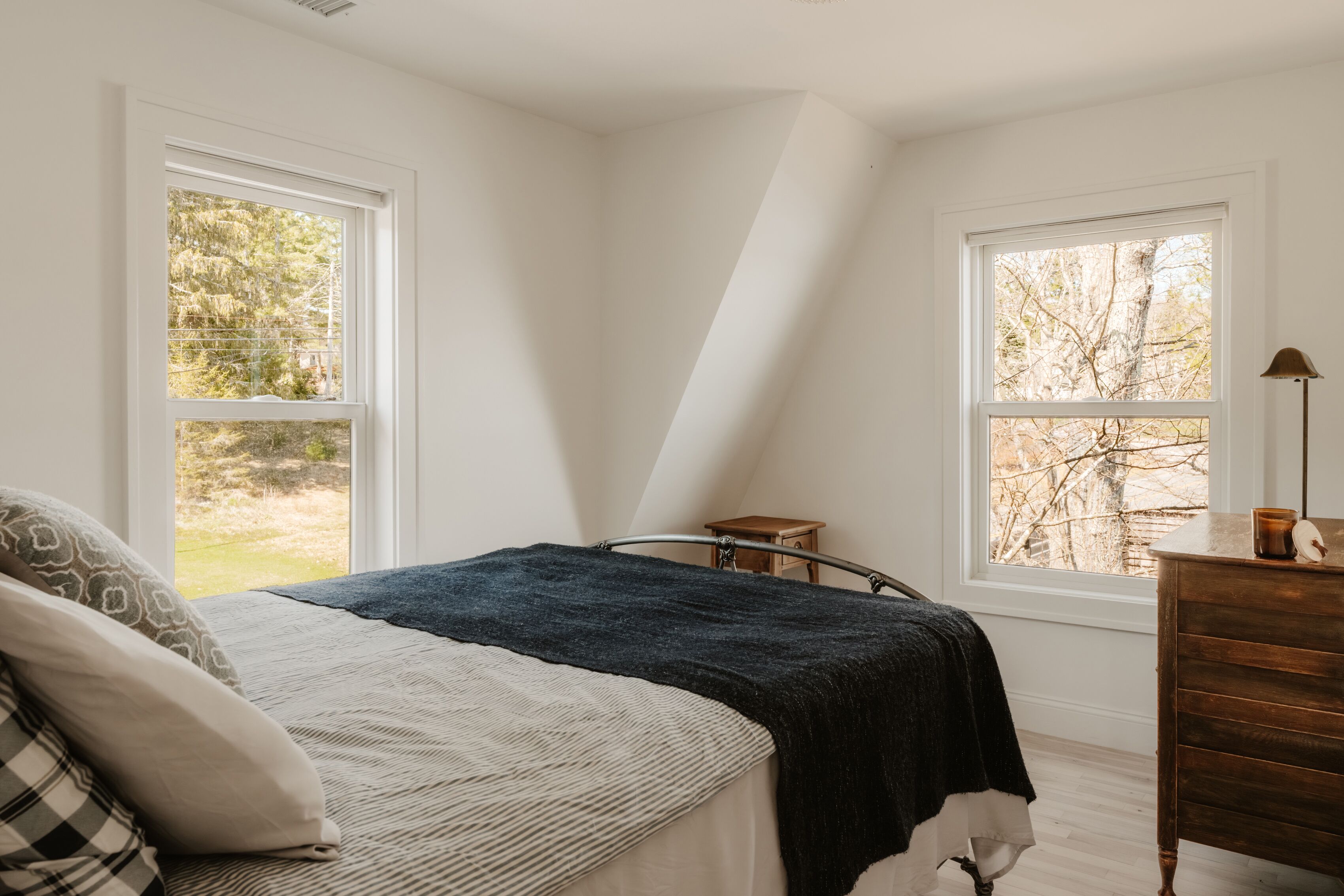 Un dormitorio con cama, dos ventanas, un tocador y una mesita de noche.