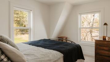 Un dormitorio con cama, dos ventanas, un tocador y una mesita de noche.