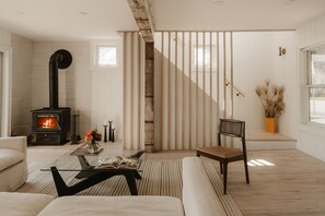 Una sala de estar moderna con una estufa de leña, una escalera y un ventanal grande.