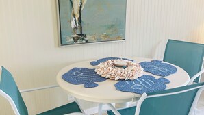 Una mesa de comedor con un cuadro de un pájaro, rodeada de sillas color turquesa y posavasos azules.