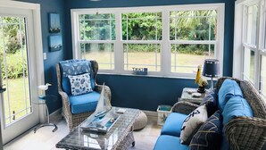 Una habitación soleada con un ventanal grande, muebles de mimbre y un ventilador de techo.