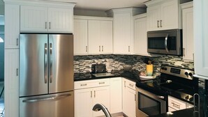 Una cocina moderna con armarios blancos, electrodomésticos de acero inoxidable y encimera negra.