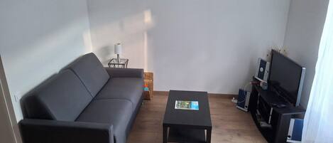 A living room with a sofa, a coffee table, a TV stand with a TV, and a bookshelf.