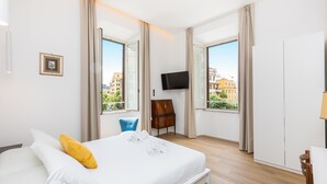 A hotel room with a bed, a TV, a chair, and large windows with a city view. - Cola di Rienzo apartment (Rome)