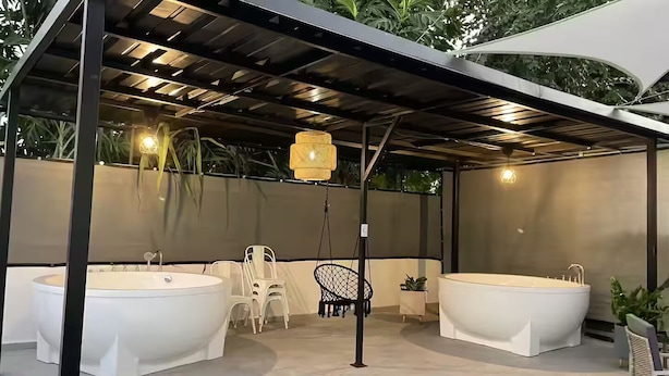 Un espace extérieur abrité comprenant deux grandes baignoires blanches, un fauteuil suspendu et une petite table agrémentée d’une plante.