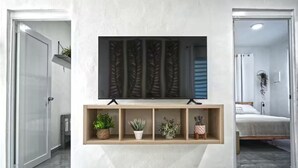 Une chambre d’hôtel moderne dotée d’un grand téléviseur à écran plat fixé au mur, au-dessus d’une étagère en bois où sont disposées des plantes en pot.