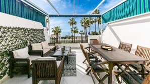 An outdoor patio with a dining area, sofas, and a view of palm trees and the sea.