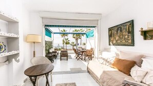A bright living room with a sofa, a coffee table, and a dining area with chairs and a table. There is a view of palm trees outside.