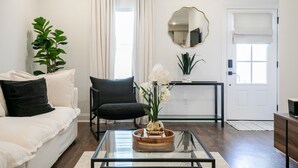 A living room with a white sofa, black chair, glass coffee table, and a wooden side table. - The Hurley, 3BR Luxe Townhouse by VelvetDitchVillas (Oxford)