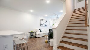 A modern living room with a white sofa, a coffee table, and a staircase with wooden steps. - The Hurley, 3BR Luxe Townhouse by VelvetDitchVillas (Oxford)
