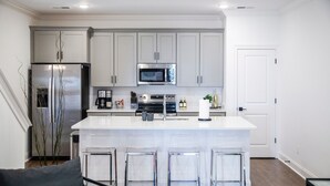 A modern kitchen with a central island, stainless steel appliances, and a white door. - The Hurley, 3BR Luxe Townhouse by VelvetDitchVillas (Oxford)