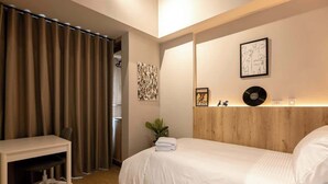 Een slaapkamer met een bed, een bureau en een stoel. Twee kunstwerken hangen aan de muur en er staat een plant.