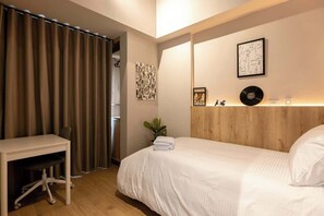 Un dormitorio con una cama, un escritorio y una silla. Hay dos obras de arte colgadas en la pared y una planta.