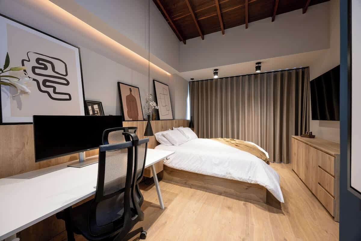 A modern bedroom with a desk, bed, and artwork on the walls.