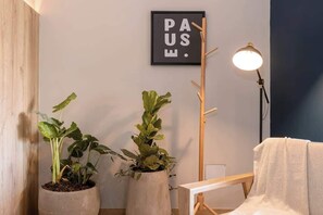 A room with two potted plants, a coat rack, a floor lamp, and a framed sign on the wall.