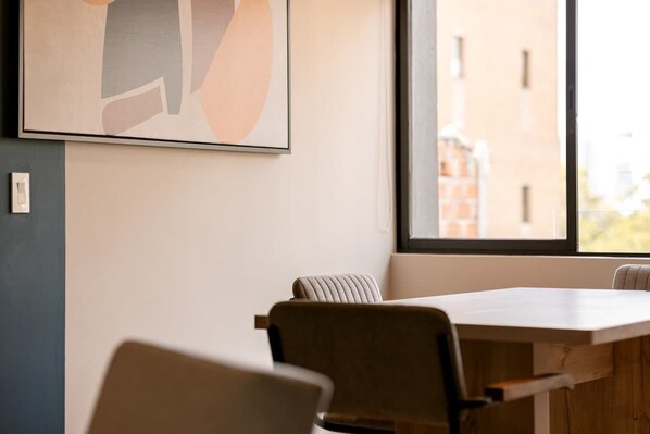 A modern office space with a large window, a framed abstract artwork, and a wooden table with chairs.