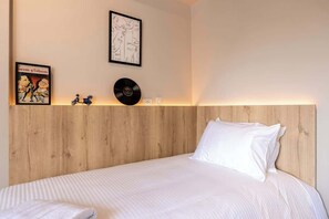 A neatly made bed with white linens, a wooden headboard, and two framed artworks on the wall.