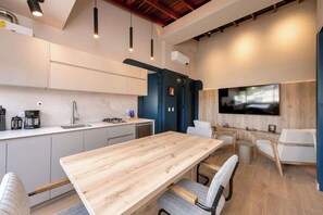 A modern kitchen with a wooden dining table and chairs, a built-in TV, and pendant lighting.