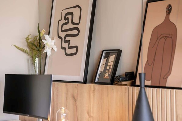 Zona de recepción con televisor de pantalla plana, un florero con flores, obras de arte enmarcadas y un mostrador de madera.