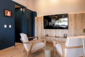 Una sala de estar moderna con un televisor de pantalla plana grande montado en la pared, muebles de madera y una pequeña mesa redonda.