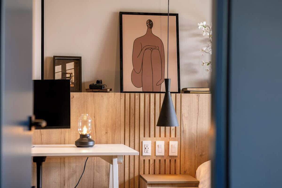 Ein modernes Zimmer mit einer Holzpaneelwand, einem gerahmten Kunstwerk mit einer menschlichen Figur, einem Schreibtisch mit einer Lampe und einer Bank.
