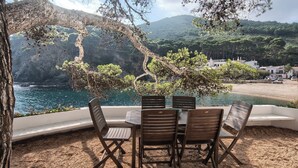 A table with four chairs and a view of a coastal landscape with trees and a mountain in the background. - 3 bedroom in first sea line in Sa Tuna, Begur H02 (Begur)