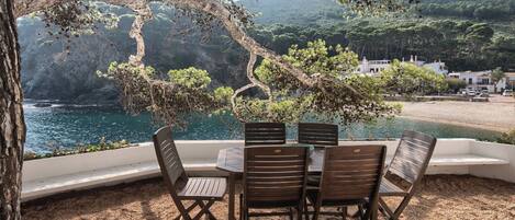 Una mesa con cuatro sillas y vistas a un paisaje costero con árboles y una montaña al fondo.