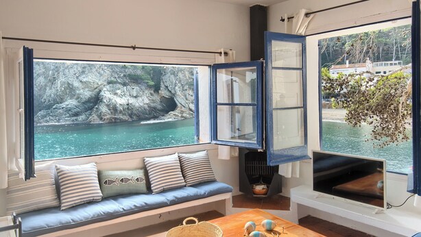 A cozy room with a large window overlooking a rocky coastline and a view of a village. - 3 bedroom in first sea line in Sa Tuna, Begur H02 (Begur)