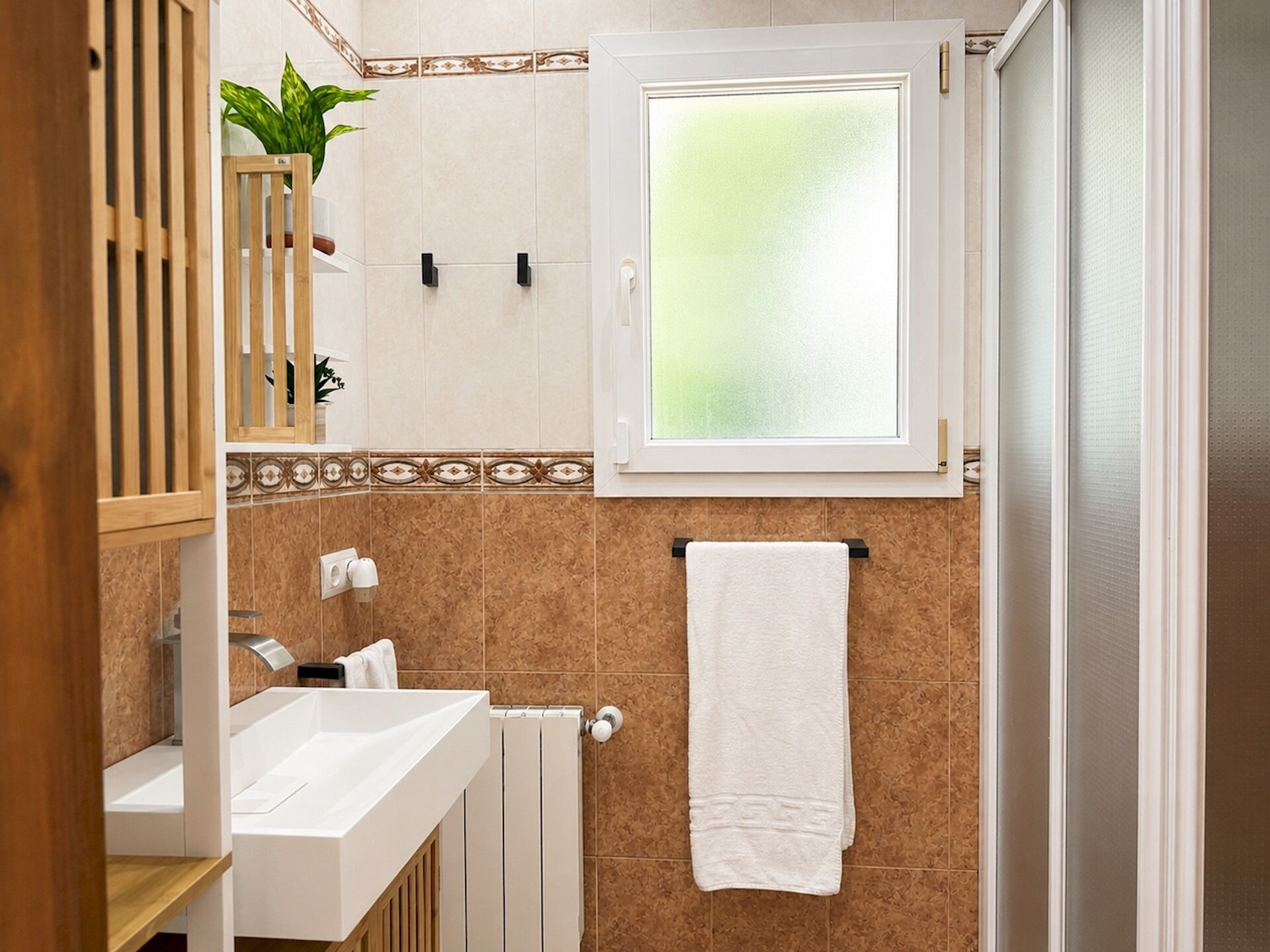 A bathroom with a white sink, a towel rack, a window with frosted glass, and a plant on the wall.