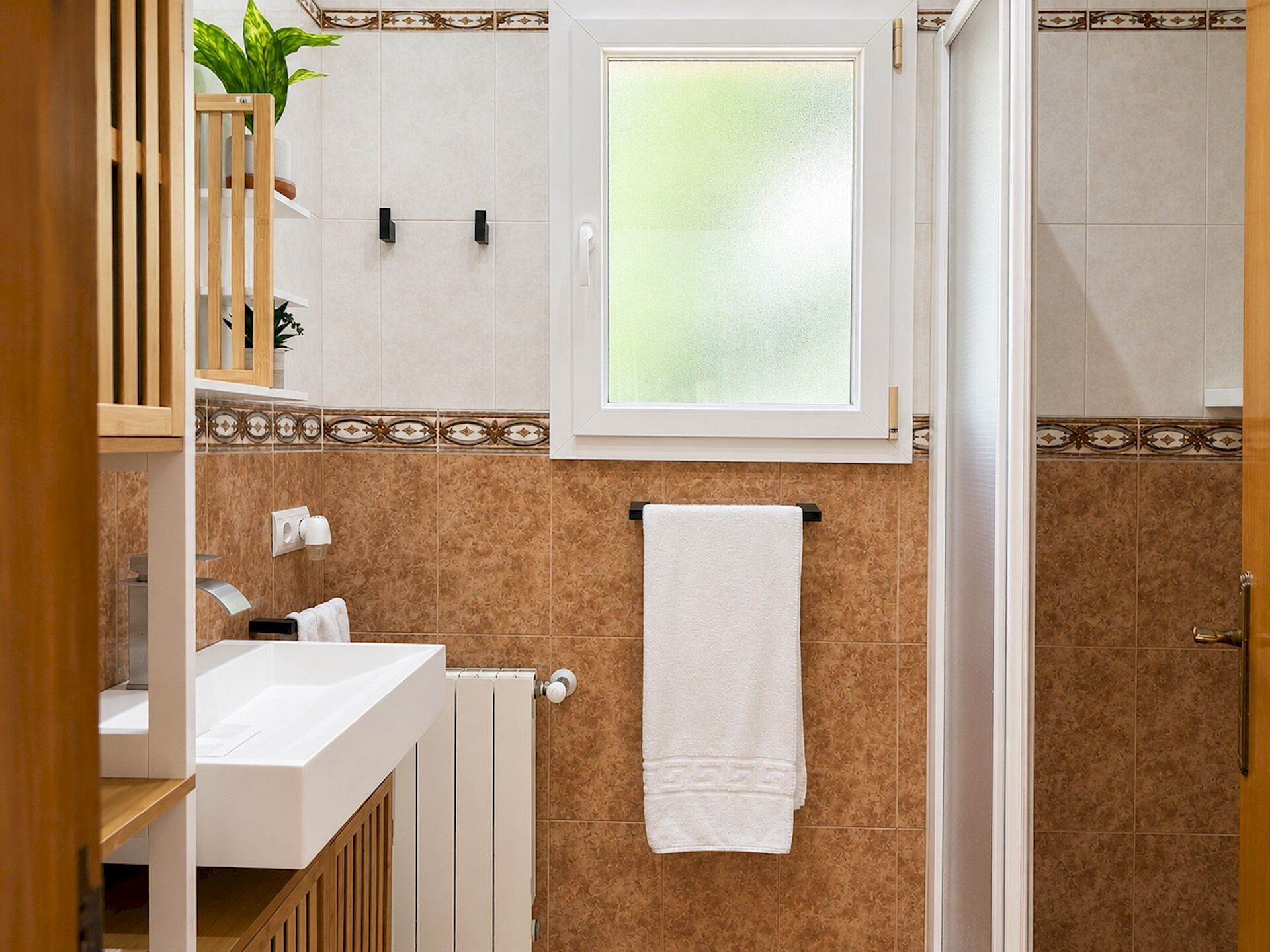 A bathroom with a white sink, a towel hanging on a rack, a radiator, and a window with frosted glass.