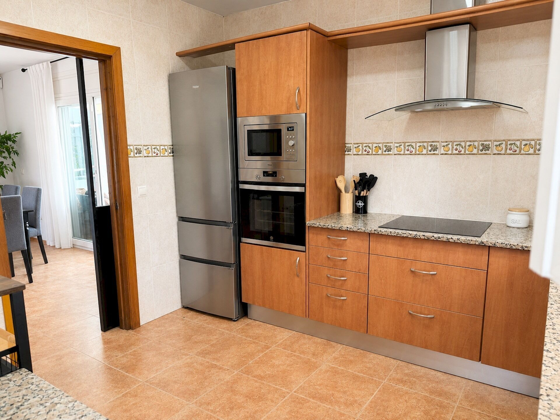 A kitchen with a refrigerator, oven, microwave, wooden cabinets, and a tiled backsplash.