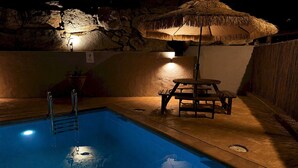 A swimming pool with a stone wall, a thatched umbrella, and a wooden table. - Villa w/ pool in Begur (H14) (Begur)