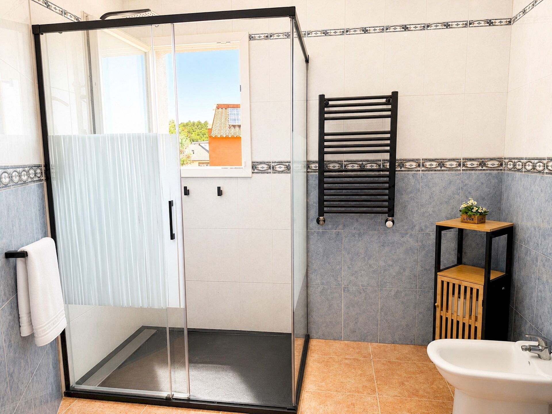 A shower with a glass door, a towel rack, a sink, and a small shelf with a plant.