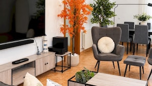 A modern living room with a flat-screen TV, a grey armchair, a coffee table, and a dining area with grey chairs. - Villa w/ pool in Begur (H14) (Begur)